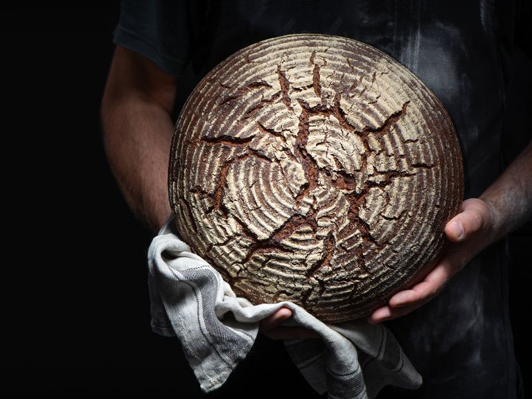 Bäckerhände halten frisch gebackenes Brot (Symbolbild) Brotlaib