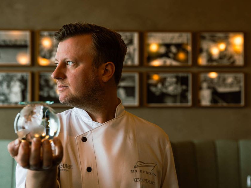 Kevin Fehling in der Küche des THE GLOBE an Bord der EUROPA mit einer gläsernen Weltkugel.