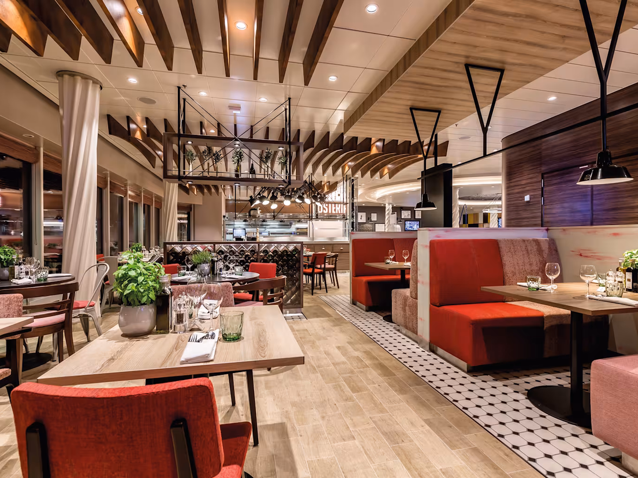 Italienisches Restaurant an Bord eines Kreuzfahrtschiffs mit Holztischen, roten Sitzbänken, Basilikumtöpfen und offener Küche im Hintergrund